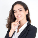 smiling young woman in a black blazer and white shirt with her hand on her chin against a white background