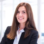 smiling young woman in a black blazer and white shirt with her hand on her chin against a white background