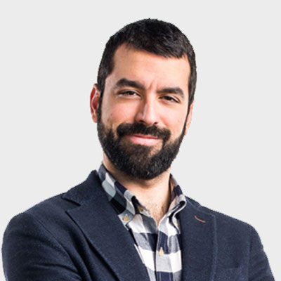man with a dark beard and short hair smiling, wearing a navy blue blazer over a black and white plaid shirt.