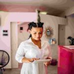 woman in a white blouse using a digital tablet while standing in a modern, brightly lit office or studio space